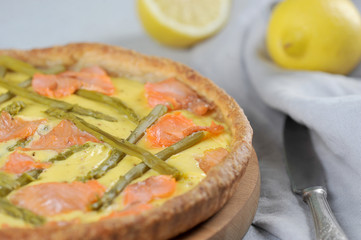 Traditional quiche with asparagus and red fish on a light background. Napkin and crowbar in the frame. Close-up.
