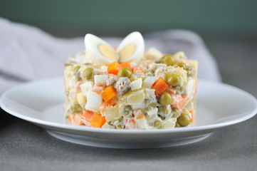 Traditional salad Russian cuisine Olivier. A portion of salad on a white plate. Close-up. Gray background.