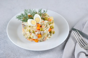 Traditional salad Russian cuisine Olivier. A portion of the salad is decorated with dill and quail egg. Close-up. Light background.