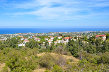 Fototapeta na wymiar Amazing view over small city Bellapais in Kyrenia region, Northern Cyprus. The view point is overlooking the Mediterranean sea and adjacent subtropical landscape. Blue sky above. Popular tourist spot