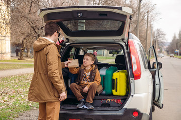 father with son packing bags to car trunk. car travel concept