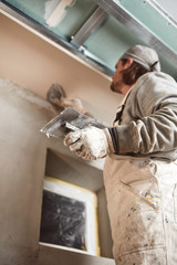 Workman plastering gypsum walls inside the house.