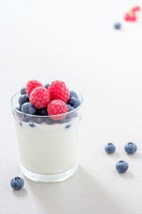 Joghurt im Glas mit gemischten Beeren auf weißem, strukturiertem Holztisch im Gegenlicht