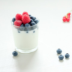 Joghurt im Glas mit gemischten Beeren auf weißem, strukturiertem Holztisch im Gegenlicht