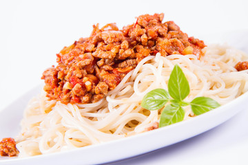 Spaghetti bolognese on a plate decorated with fresh basil in a white background