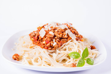Spaghetti bolognese on a plate decorated with parmesan  cheese and fresh basil in a white background