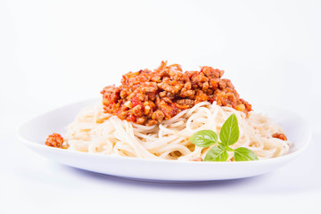 Spaghetti bolognese on a plate decorated with fresh basil in a white background