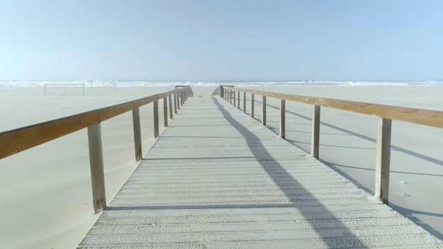 POV stabilized camera moving through empty wooden boardwalk at beach on warm summer day. Beautiful calm and tranquil escapeist shot of quiet futuristic travel destination place, meditation or yoga