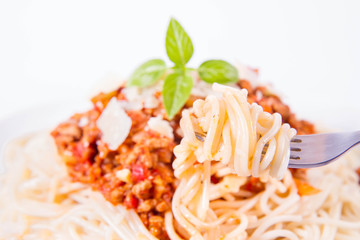 Spaghetti bolognese on a plate decorated with parmesan  cheese and fresh basil eaten with a fork