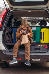 little kid looking into paper bag with candies sitting in car trunk