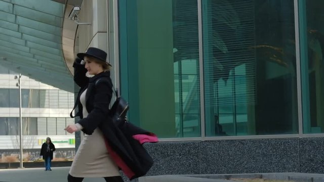 blond girl with backpack walks putting on hat in street