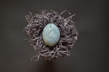 Gray egg with crack, painted in tea hibiscus, lies on paper similar to a nest of hay on gray...