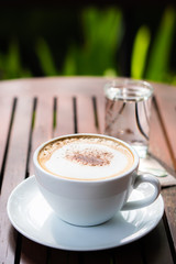 Hot coffee placed on the wooden table in early morning with copyspace, white cup and silver spoon. The green background with defocus effect.