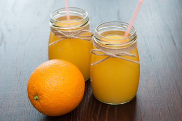 Fototapeta na wymiar Orange juice and whole orange in two jars rustic style side view, copy space