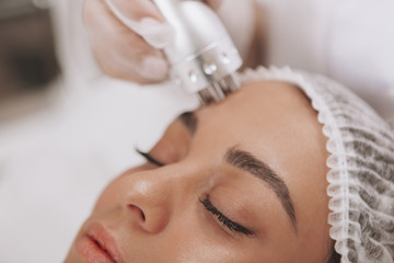 Cropped close up of a beautiful woman getting facial treatment at beauty clinic. Cosmetologist using hardware skincare equipment. Beautician performing microcurrent therapy on female patient