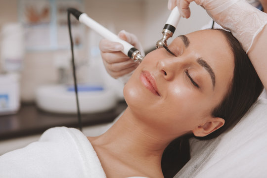 Stunning young woman with flawless skin enjoying facial treatment at cosmetology clinic. Relaxed beautiful female patient visiting dermatologist, getting microcurrent face therapy