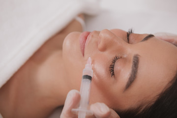 Obraz na płótnie Canvas Attractive woman getting facial injections at cosmetology clinic. Attractive woman receiving hyaluronic acid injections by professional dermatologist. Rejuvenation concept
