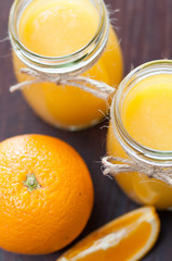 Orange, slice and juice in jars on a dark wooden table, rustic style top view, copy space, vertical format