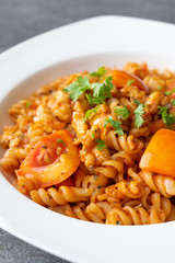 Spiral pasta in sauce tomato with chicken in white dish on concrete table.