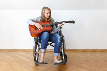 Disabled young woman in wheelchair playing the guitar.