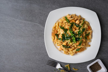 Spiral pasta in fried basil with chicken in white dish on concrete table.