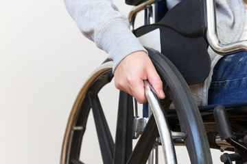 Detail of disabled woman holding a hand on wheel of a wheelchair.