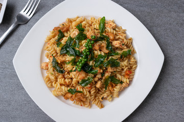 Spiral pasta in fried basil with chicken in white dish on concrete table.