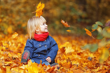 Happy autumn! Little sweet girl playing with leaves in an autumn park. Copy space, falling leaves.