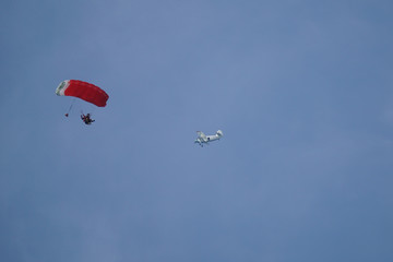    Tandem skydiver is flying with parachute in blue sky.  Airplane in the background