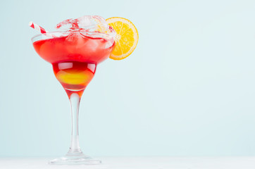 Tropical alcohol sunrise drink - red, yellow liquor, oranges slice, straw, ice in misted glass on elegant green background.