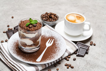 Classic tiramisu dessert in a glass and cup of coffee on concrete background