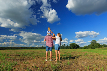 Mom dad and daughter look at the sun in the wheat field. Back view.