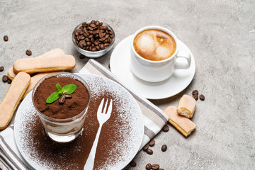 Classic tiramisu dessert in a glass and cup of coffee on concrete background