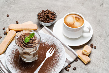 Classic tiramisu dessert in a glass and cup of coffee on concrete background