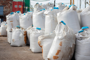 Large white bags of salt lie on the street. Industrial fertilizers are stored in bags in a heap. Rusty stains on the package.