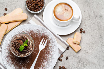 Classic tiramisu dessert in a glass and cup of coffee on concrete background