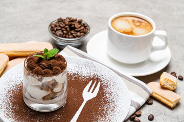 Classic tiramisu dessert in a glass and cup of coffee on concrete background