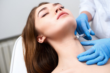 Beautician doctor with botulinum toxin syringe making injection to platysmal bands. Neck...