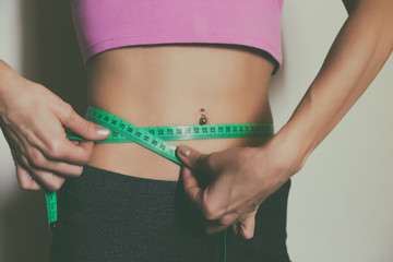 Fit woman measuring her thin waist  with a tape measure.Toned photo.