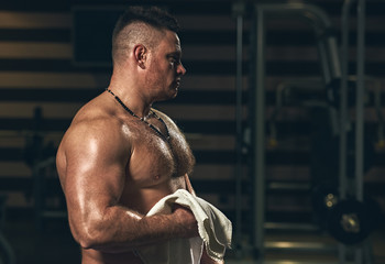Muscular tired bodybuilder with white towel resting after training