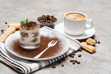 Classic tiramisu dessert in a glass and cup of coffee on concrete background