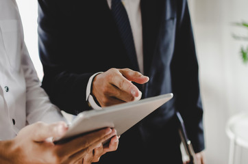 two young business man investor in suit talking and reading information about financial news in mobile tablet together standing in modern office, finance, investment and digital technology concept