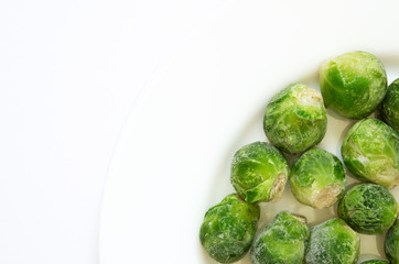 Frozen Brussels sprouts on a white plate. Top view, flat lay, copy space.