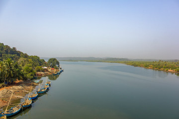 Indian workers extract sand in a river way, an aerial view of large blue boats at the shore and green palm trees