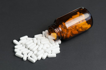 White Calcium Pills Pouring Out Of Glass Bottle. Calcium Supplement Tablets On Dark Background.