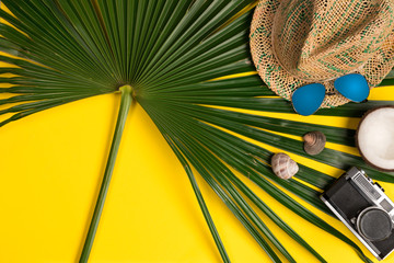 Top view of palm leaves, hat, vintage sunglasses and coconut on yellow background. Flat lay. Travel concept, empty space for text