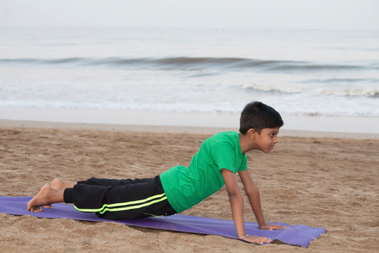 Boy practicing yoga cobra pose on the beach