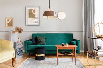 Stylish and elegant living room of apartment interior with green velvet armchair and sofa, brwon table, plant, design lamp and chic accessories. Abstract paintings on the gray wall. Luxury home decor.