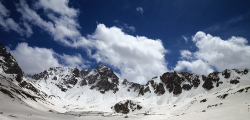 Panoramic view on high snowy mountains and blue cloudy sky