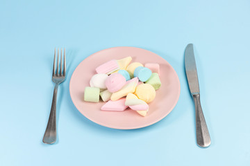 Plate with marshmallow, fork, knife  isolated on blue background.